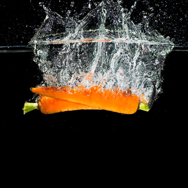 Twee oranje wortelen die in waterplons vallen
