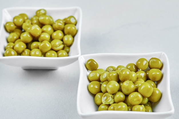 Twee platen van gekookte groene erwten op een grijze tafel.