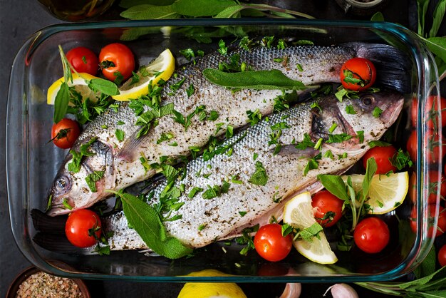 Twee rauwe zeebaars in een ovenschaal met kruiden op een zwarte tafel. Bovenaanzicht