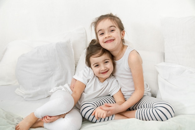 Twee schattige kleine zusjes meisjes knuffelen op het bed in de slaapkamer. Het concept van familiewaarden en de vriendschap van kinderen.