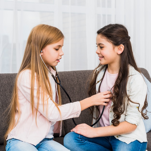 Twee schattige meisjes spelen arts en ziekenhuis met behulp van stethoscoop