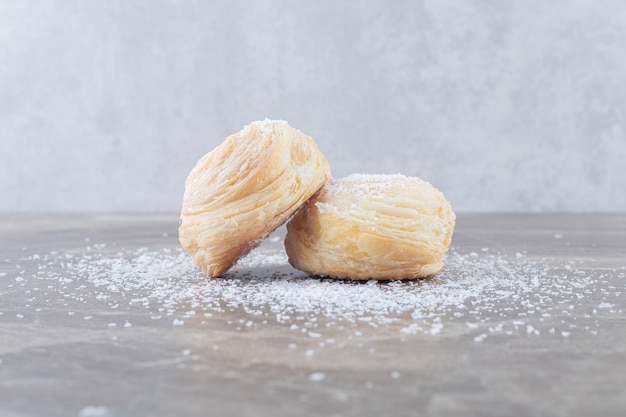 Twee schilferige koekjes bedekt met vanillepoeder op marmeren oppervlak