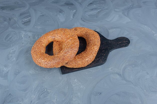 Twee sesam bedekt bagels op een zwarte houten bord op marmeren oppervlak.