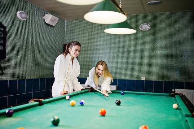 Twee sexy meiden in witte badjas spelen poolbiljart