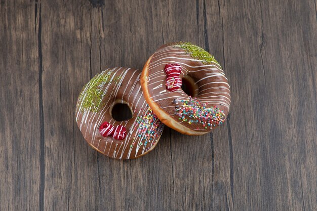 Twee smakelijke donuts met chocolade glazuur op houten tafel.