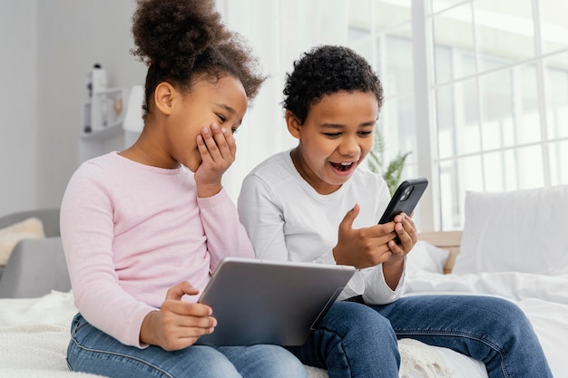 Twee smiley broers en zussen thuis samen spelen op tablet en smartphone