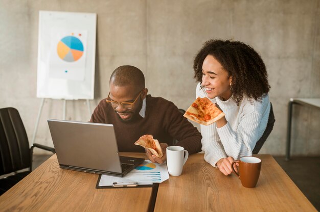 Twee smileycollega's die pizza hebben tijdens een onderbreking van de bureauvergadering