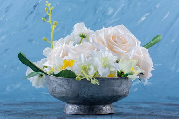 Twee soorten bloemen geplaatst in metalen kom op blauw.