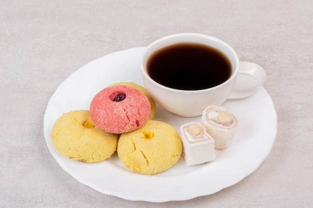 Twee soorten koekjes, lekkernijen en kopje thee op witte plaat.