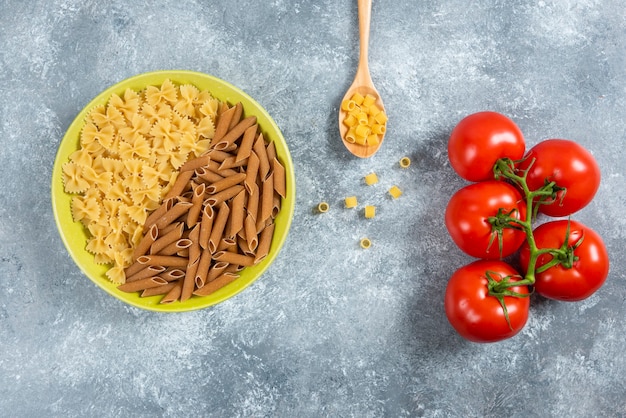 Gratis foto twee soorten rauwe pasta op plaat met tomaten.