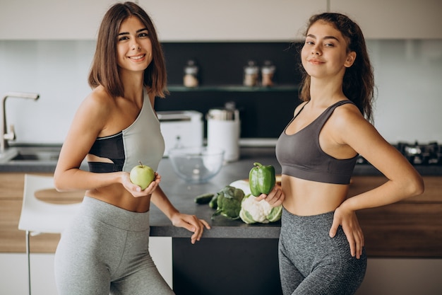 Twee sportieve meisjes die bij keuken voedsel bereiden