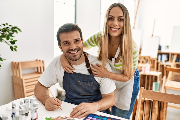 Twee studenten glimlachend gelukkig schilderij zittend op de tafel op de kunstacademie.