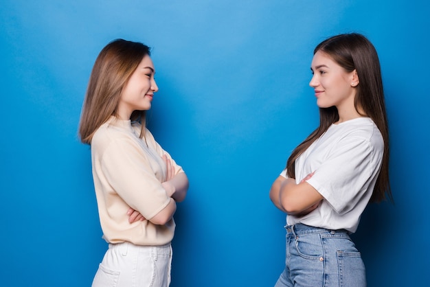 Twee tevreden meisjes kijken elkaar aan over een blauwe muur
