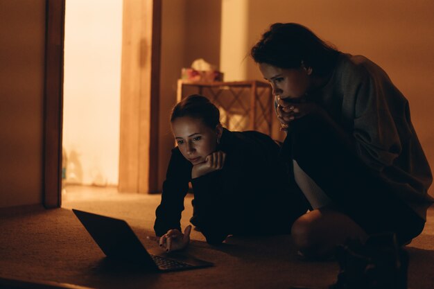 Twee tienerjaren die op online inhoud letten in laptop die op de vloer ligt