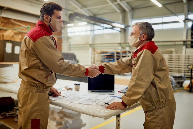 Twee timmerlieden met gezichtsmaskers die elkaar feliciteren met een succesvol project in een werkplaats