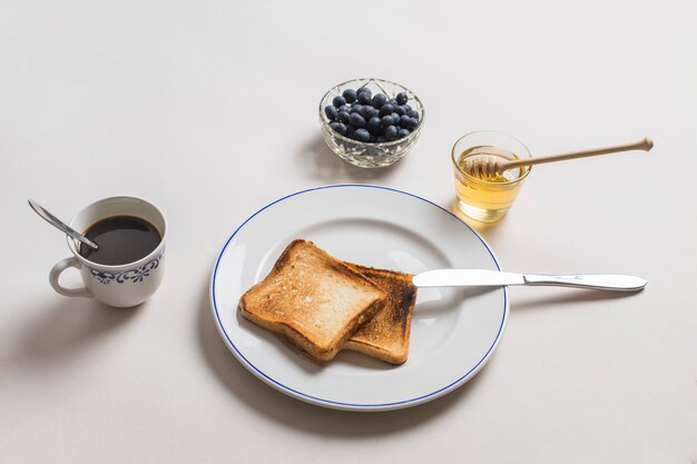Twee toast brood met honing; thee en bosbessen op witte achtergrond