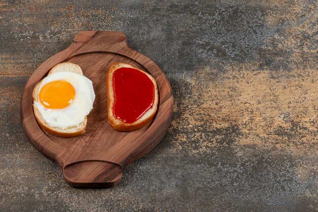 Twee toastbrood met gebakken ei en jam op houten plaat.