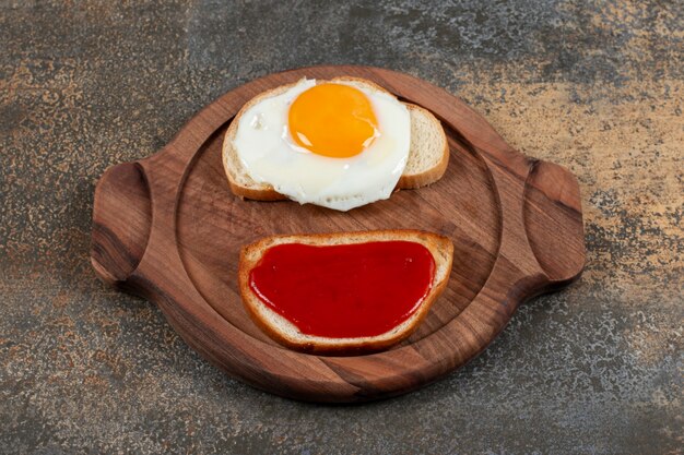 Twee toastbrood met gebakken ei en jam op houten plaat.