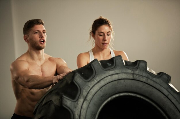 Twee toegewijde atleten doen een oefening voor het omdraaien van banden terwijl ze cross-training hebben in een gezondheidsclub