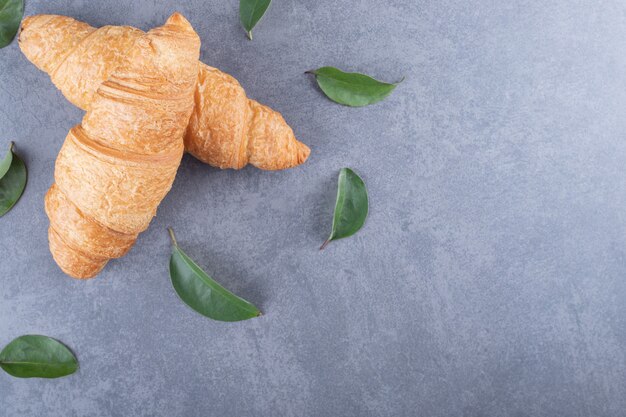 Twee verse Franse croissant met decoratieve bladeren op een grijze achtergrond