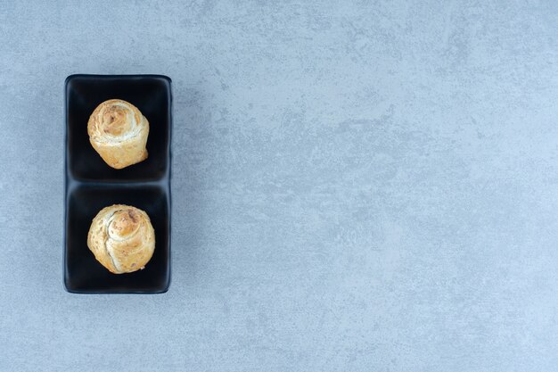 Twee verse koekjes op zwarte plaat over grijze achtergrond.