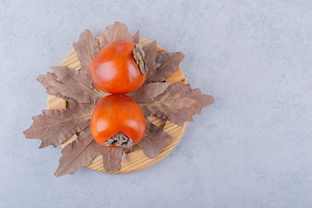 Twee verse persimmon vruchten en gedroogde bladeren op houten plaat.