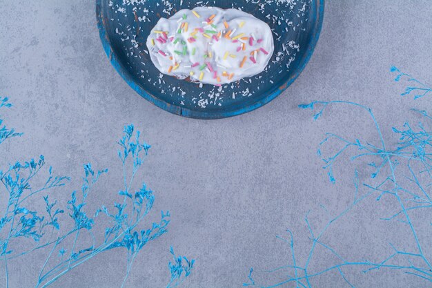Twee verse zoete cupcakes met kleurrijke hagelslag en room op een blauwe houten bord.