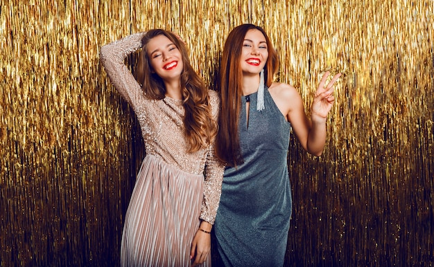 Twee vierende meisjes in het elegante avondjurk stellen op gouden opeenvolging