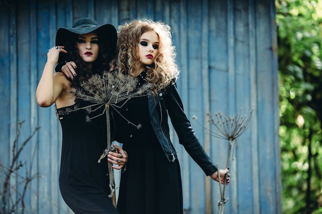 Twee vintage vrouwen als heksen, poseren voor een verlaten huis aan de vooravond van Halloween