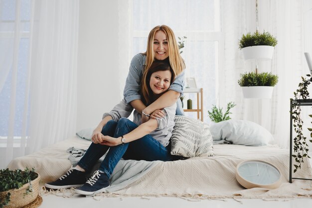 Twee volwassen zussen knuffelen elkaar zacht zittend op het witte bed