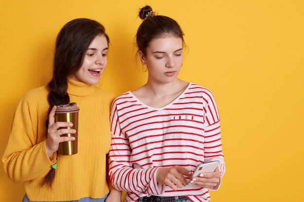 Twee vrienden die slimme telefoon delen en samen koffie drinken, het stellen