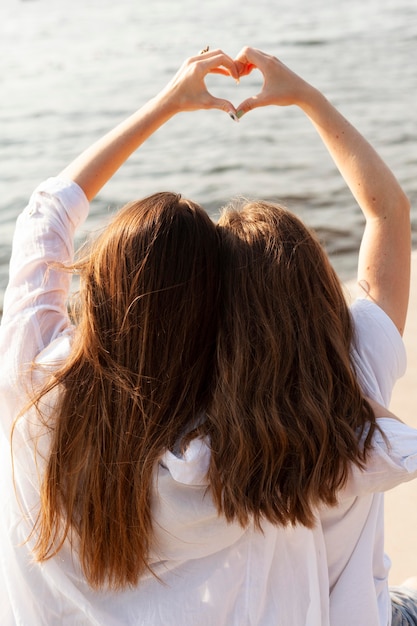 Gratis foto twee vriendinnen die het liefdeteken maken bij het meer