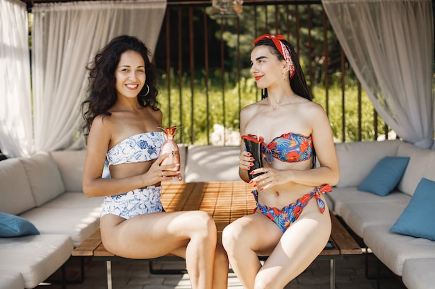 Twee vriendinnen in een badmode zitten in bungalow. Meisjes die blauwe en rode zwemkleding dragen