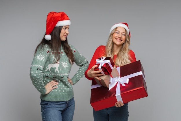 Twee vriendinnen met nieuwjaarsgeschenken op grijze achtergrond met kopieerruimte, alle cadeautjes in één hand