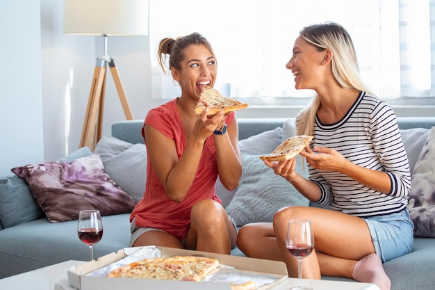 Twee vriendinnen roddelen met glazen rode wijn en pizza's Afbeeldingen tonen aan haar vriend op haar sociale netwerk op de mobiele telefoon