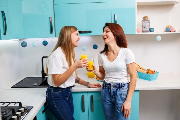 Twee vriendinnen staan in de keuken en drinken sinaasappelsap. vriendinnen chatten en delen geheimen in de keuken, ontbijt