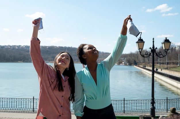 Twee vriendinnen vieren samen buitenshuis het opheffen van de beperkingen van gezichtsmaskers