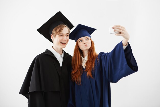Twee vrolijke afgestudeerden van de universiteit gek maken selfie.