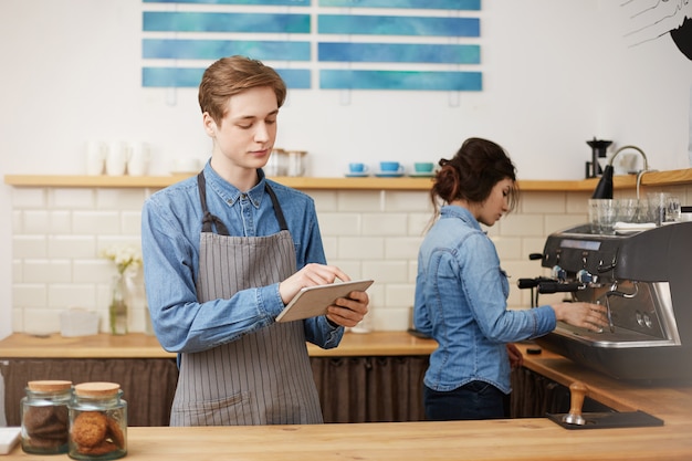 Gratis foto twee vrolijke barista's in stijlvol uniform wroking aan toog.