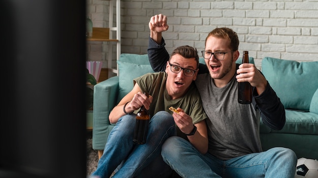 Twee vrolijke mannelijke vrienden kijken naar sport op tv en bier drinken