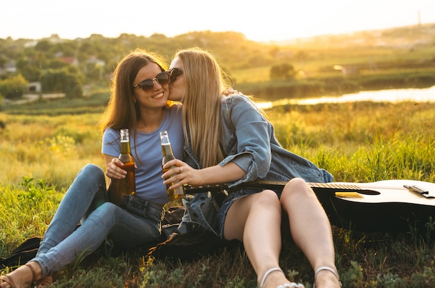 Twee vrolijke meisjes en jonge vrienden met een zonnebril, bier drinken en genieten van de tijd samen doorgebracht bij zonsondergang.