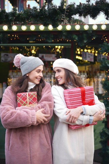 Twee vrolijke vrouwen met cadeautjes op kerstmarkt