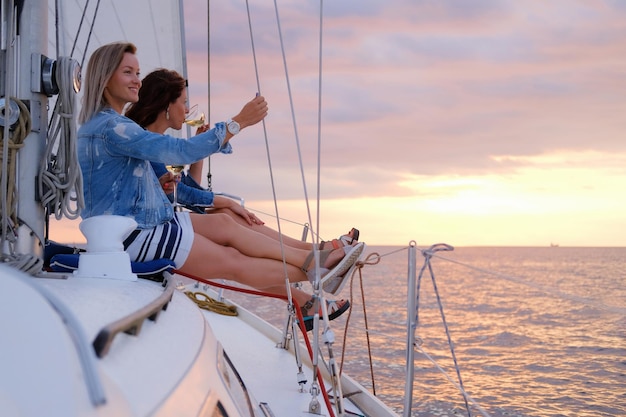 Twee vrolijke vrouwen vieren een goede zomerdag op het jacht terwijl ze naar de prachtige zonsondergang kijken.