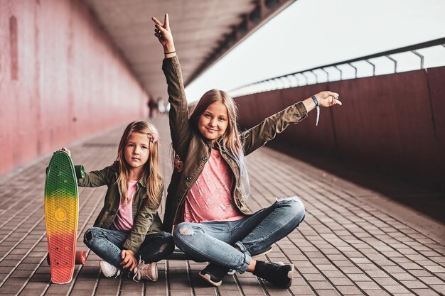 Twee vrolijke zusjes zitten op het skateboard in de tunnel.