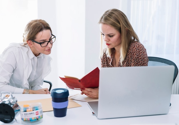 Twee vrouwelijk zakenlui die agenda in bureau lezen
