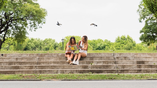 Twee vrouwelijke toeristenzitting op trap het bekijken kaart in het park