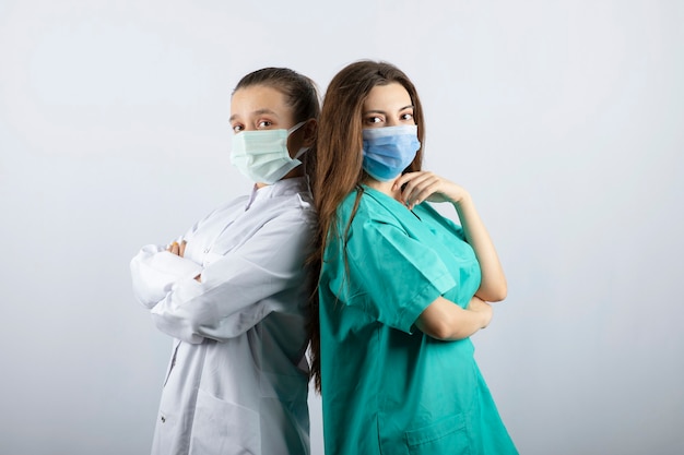 Twee vrouwelijke verpleegsters met medische maskers die naar de camera kijken