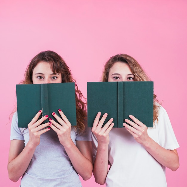 Gratis foto twee vrouwelijke vrienden die hun gezicht behandelen met groen dekkingsboek tegen roze achtergrond