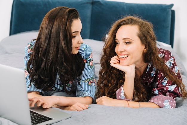 Twee vrouwelijke vrienden die op bed met laptop liggen