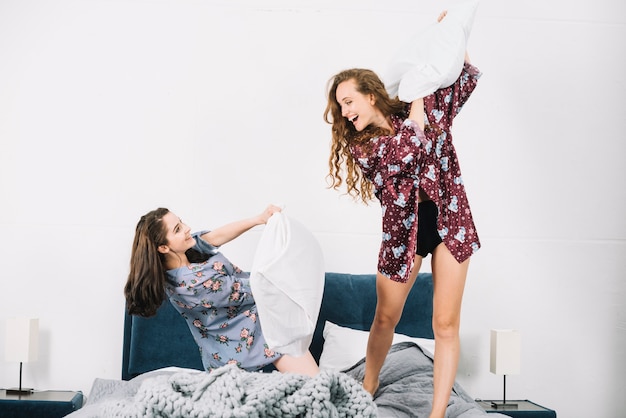 Twee vrouwelijke vrienden die pret met hoofdkussen op bed hebben